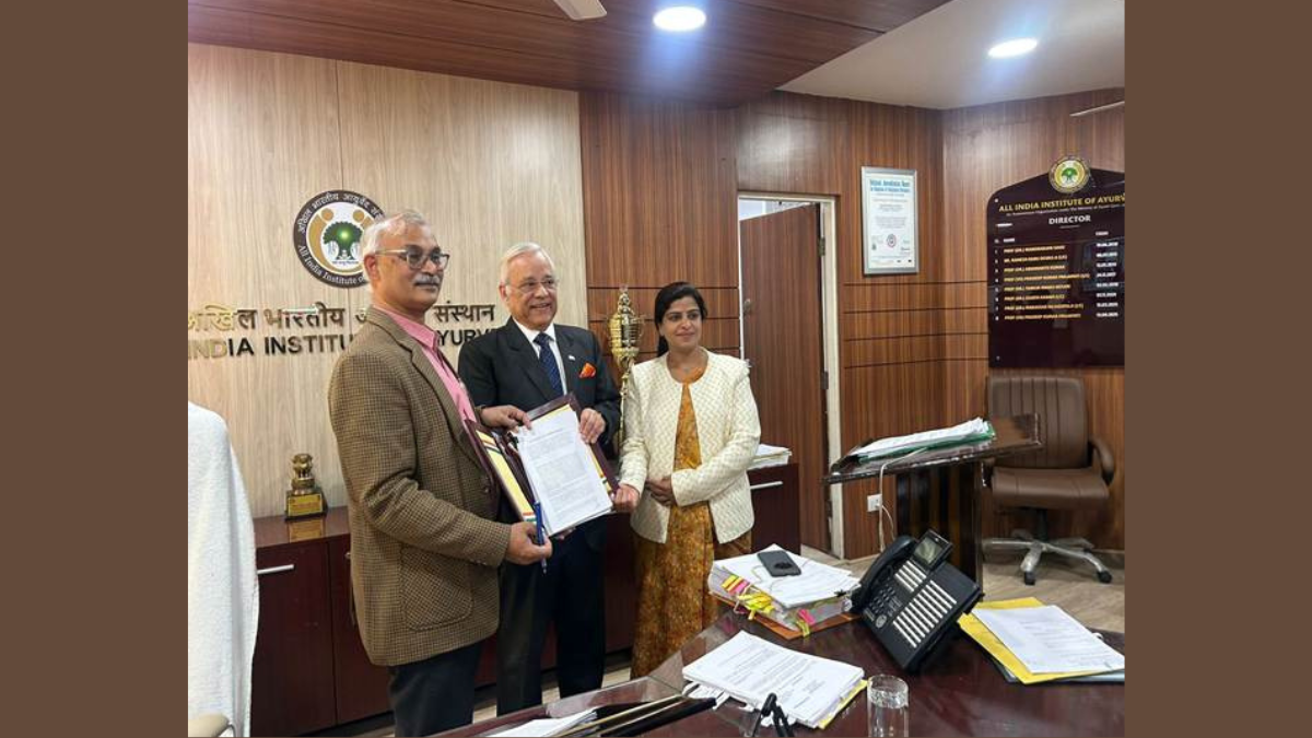 Prof. (Vd.) P.K. Prajapati and Shri Segar Sampathkumar shaking hands across a conference table, flanked by the official AIIA and GIC delegation under portraits of Indian leadership.