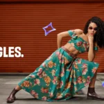A vibrant fashion advertisement for the brand OWND! featuring a young woman in a teal floral crop top and high-waisted skirt posing against an orange industrial backdrop with the tagline "NO BAD ANGLES" and "BRING THE HYPE."