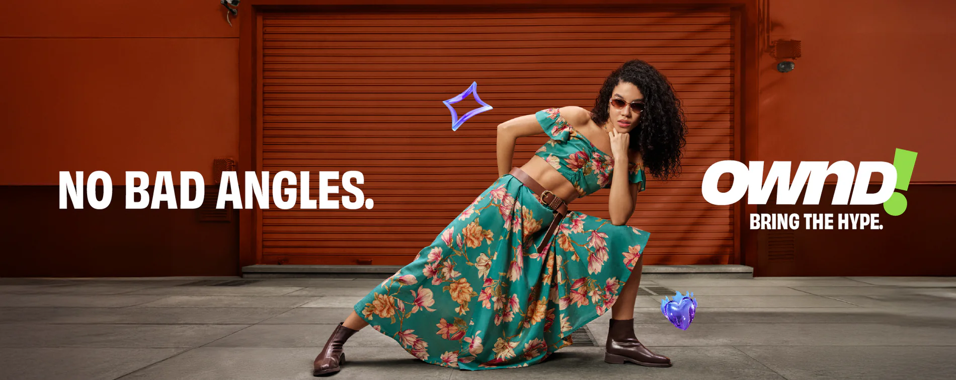 A vibrant fashion advertisement for the brand OWND! featuring a young woman in a teal floral crop top and high-waisted skirt posing against an orange industrial backdrop with the tagline "NO BAD ANGLES" and "BRING THE HYPE."