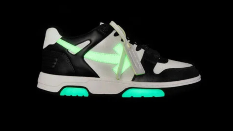 A profile view of the Off-White "Out Of Office" (OOO) sneaker in a black and white colorway featuring neon green glow-in-the-dark accents on the arrow motif and sole.