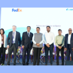 A groundbreaking ceremony for the FedEx automated air cargo hub at Navi Mumbai International Airport. The photo features Maharashtra CM Devendra Fadnavis, FedEx CEO Raj Subramaniam, Adani Airport Holdings Director Jeet Adani, and other senior officials standing before a backdrop showcasing a FedEx aircraft and the CIDCO and Adani logos.