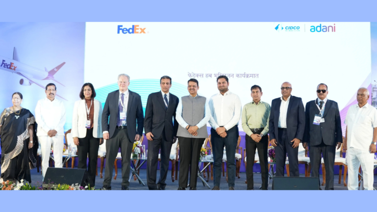 A groundbreaking ceremony for the FedEx automated air cargo hub at Navi Mumbai International Airport. The photo features Maharashtra CM Devendra Fadnavis, FedEx CEO Raj Subramaniam, Adani Airport Holdings Director Jeet Adani, and other senior officials standing before a backdrop showcasing a FedEx aircraft and the CIDCO and Adani logos.