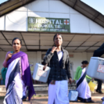 A group of female healthcare workers in sarees carrying blue medical vaccine carrier boxes outside a rural hospital in India, featuring the U-WIN logo.