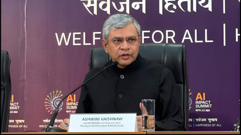 Union Minister Ashwini Vaishnaw speaking at the AI Impact Summit 2026, seated behind a nameplate with the summit branding in the background.
