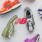 A top-down lifestyle arrangement of the New Balance Made in USA Spring/Summer 2026 footwear collection featuring vibrant purple, orange, olive green, and blue 99X series sneakers surrounding a red New Balance logo.