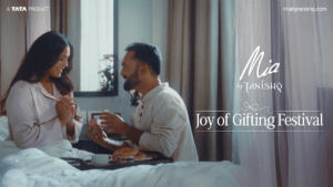 A romantic lifestyle image for Mia by Tanishq's Joy of Gifting Festival featuring a man surprising a woman with a jewelry ...