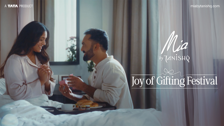 Paris Couture to Your Wardrobe: The Magic of Mia’s Cupid Edit 3.0 Launch 1 A romantic lifestyle image for Mia by Tanishq's Joy of Gifting Festival featuring a man surprising a woman with a jewelry gift box during breakfast in bed.