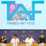 A panel of six officials seated at a press conference table under a large screen displaying the "TAF TRIBES ART FEST" logo featuring colorful tribal motifs.