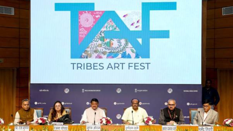 A panel of six officials seated at a press conference table under a large screen displaying the "TAF TRIBES ART FEST" logo featuring colorful tribal motifs.