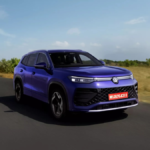 A side-profile action shot of the new Volkswagen Tayron R-Line in Nightshade Blue Metallic driving on an open Indian road, featuring the illuminated VW logo and sporty R-Line bumper.