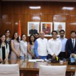 A group of diverse international students standing with Indian officials in a formal wood-paneled office under portraits of Indian leaders for the ICCR scholarship program.
