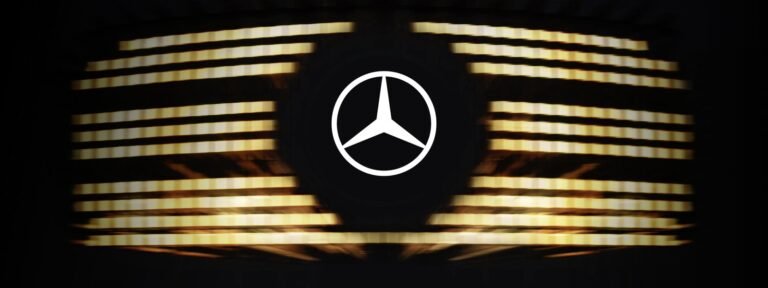 The iconic Mercedes-Benz three-pointed star logo set against a backdrop of illuminated horizontal slats, representing the upcoming 2026 V-Class.