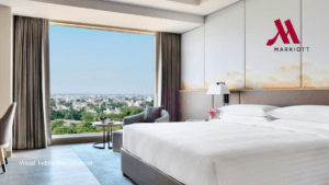 A bright, modern luxury bedroom at the Indore Marriott Hotel in India featuring floor-to-ceiling windows with a wide city ...