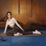 Actress Jade Picon stretching on a gym mat wearing the bold leopard-print adidas Optimé leggings and a white long-sleeve crop top.