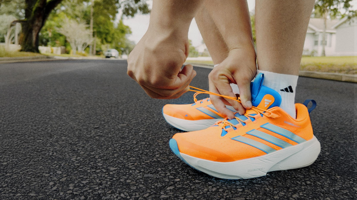 adidas Supernova Rise 3 Adaptive: A New Era of Inclusive Performance Running 2 A close-up of hands adjusting the magnetic toggle and low-pressure lacing system on an orange adidas Supernova Rise 3 Adaptive shoe.
