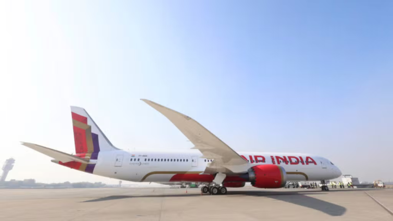 Side profile of an Air India Boeing 787 Dreamliner featuring the new global livery parked on an airport tarmac under a clear blue sky.