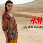 A fashion model wearing a colorful patterned bohemian-style dress from the H&M Spring/Summer 2026 collection in a desert landscape setting.