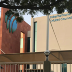 The exterior of the International Cricket Council (ICC) headquarters building in Dubai, featuring the prominent green and blue ICC logo and clear corporate branding.