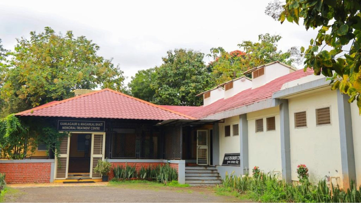 Empowering the Elderly: Vice President Inaugurates "Ayush-60" Wellness Wing at Nisargopachar Ashram 2 Exterior view of the Kamlagauri and Maganlal Bhatt Memorial Treatment Centre building at Nisargopchar Ashram with a red-tiled roof and garden.
