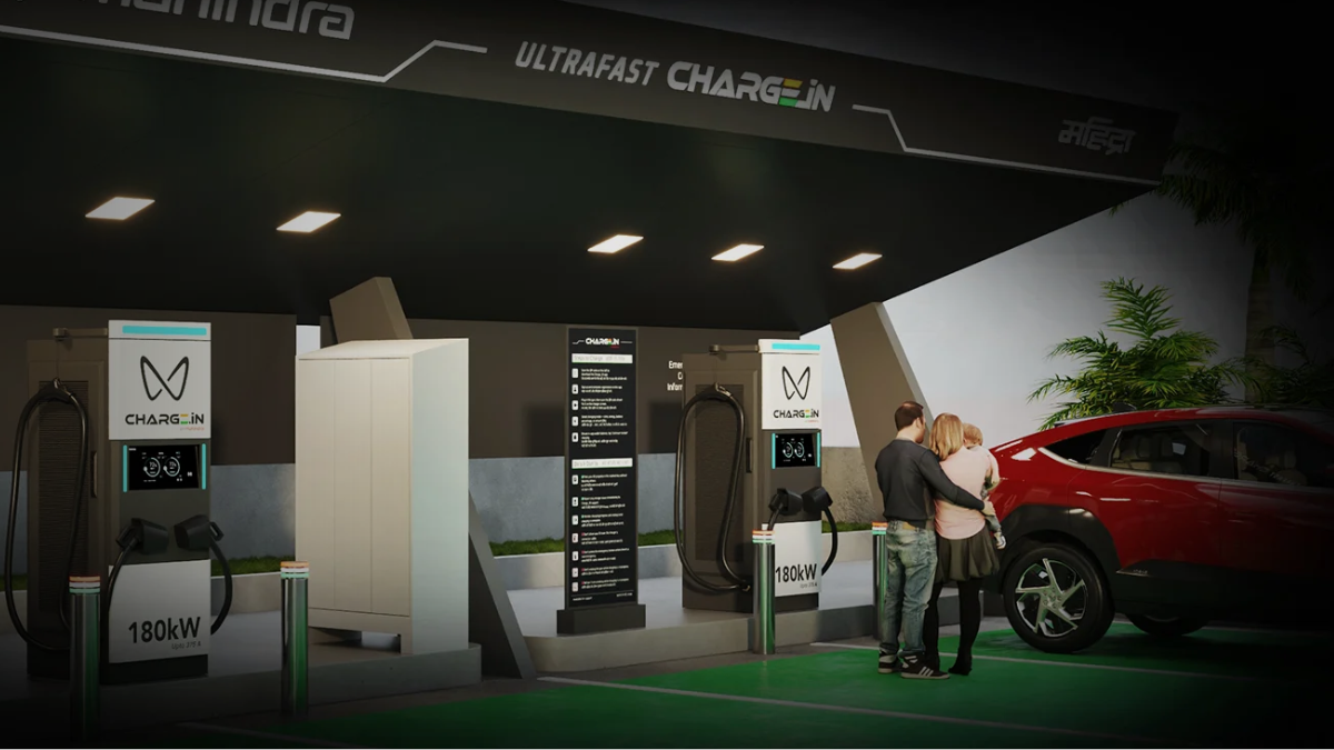 A family standing by a red electric car at a premium Mahindra Charge_iN station featuring 180kW ultra-fast dual-gun EV chargers under a modern canopy.