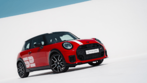 Front three-quarter view of the new MINI Cooper S Victory Edition in Chili Red with white racing stripes and the iconic 52...