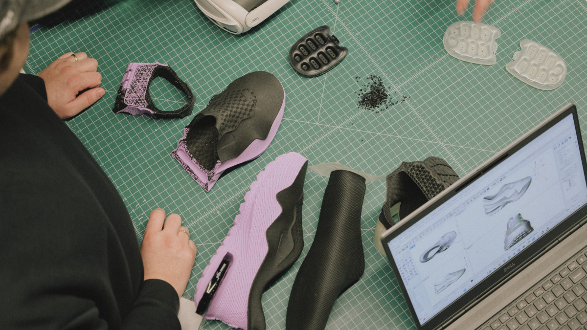 An overhead view of a Nike design desk showing a laptop with 3D CAD models, purple outsoles, and transparent Air units.
