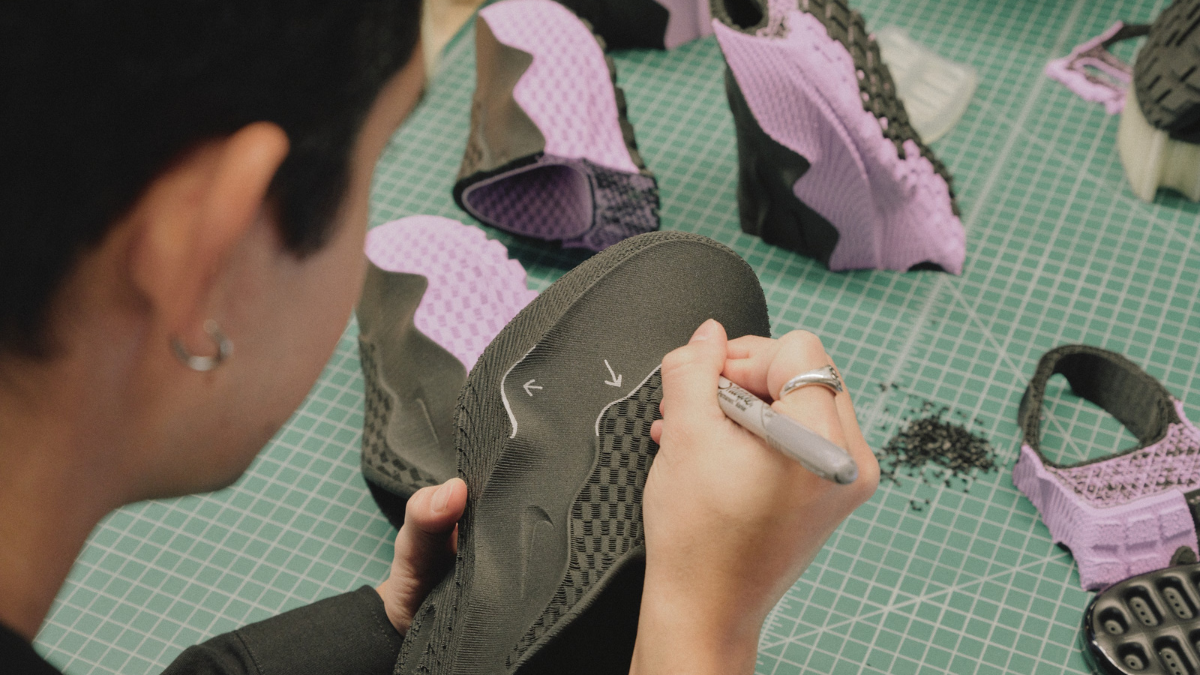 A footwear designer using a silver marker to add technical lines to a black 3D-printed sneaker upper on a green cutting mat.