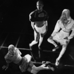 Three women posing in a high-contrast, noir-style studio setting wearing the Nike First Sight collection, including sporty cropped jackets, shorts, and futuristic footwear.