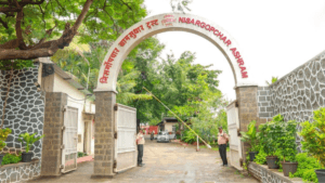 The main entrance arch of Nisargopchar Ashram in Uruli Kanchan, Pune, featuring signs in Marathi and English with security...