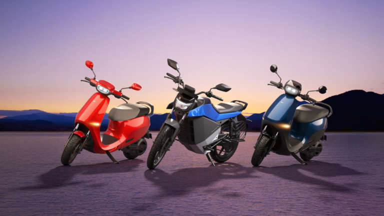 A red Ola S1 X scooter, a blue and grey Roadster X motorcycle, and a blue S1 X scooter parked against a sunset horizon.