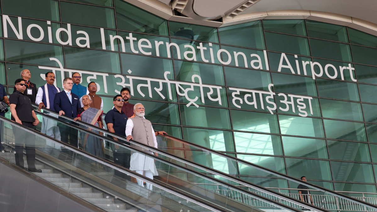 UP Takes Flight: PM Modi Inaugurates Phase I of Noida International Airport at Jewar 1 Prime Minister Narendra Modi and Uttar Pradesh officials on an escalator in front of the large "Noida International Airport" signage in English and Hindi.