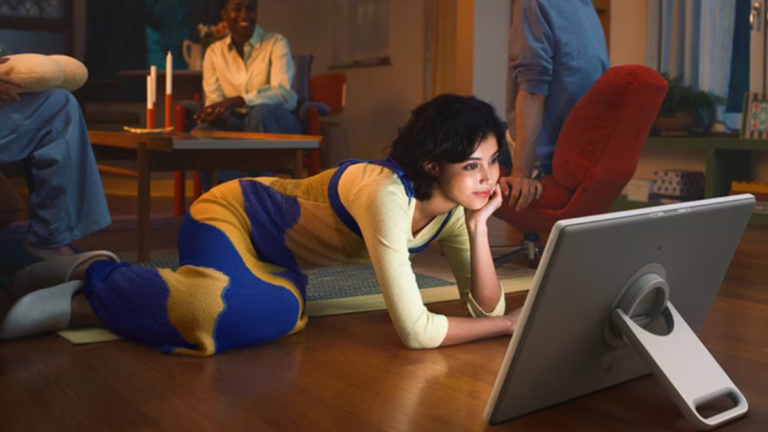 A woman lying on a living room floor using the detached 27-inch Samsung Movingstyle display with its built-in kickstand.