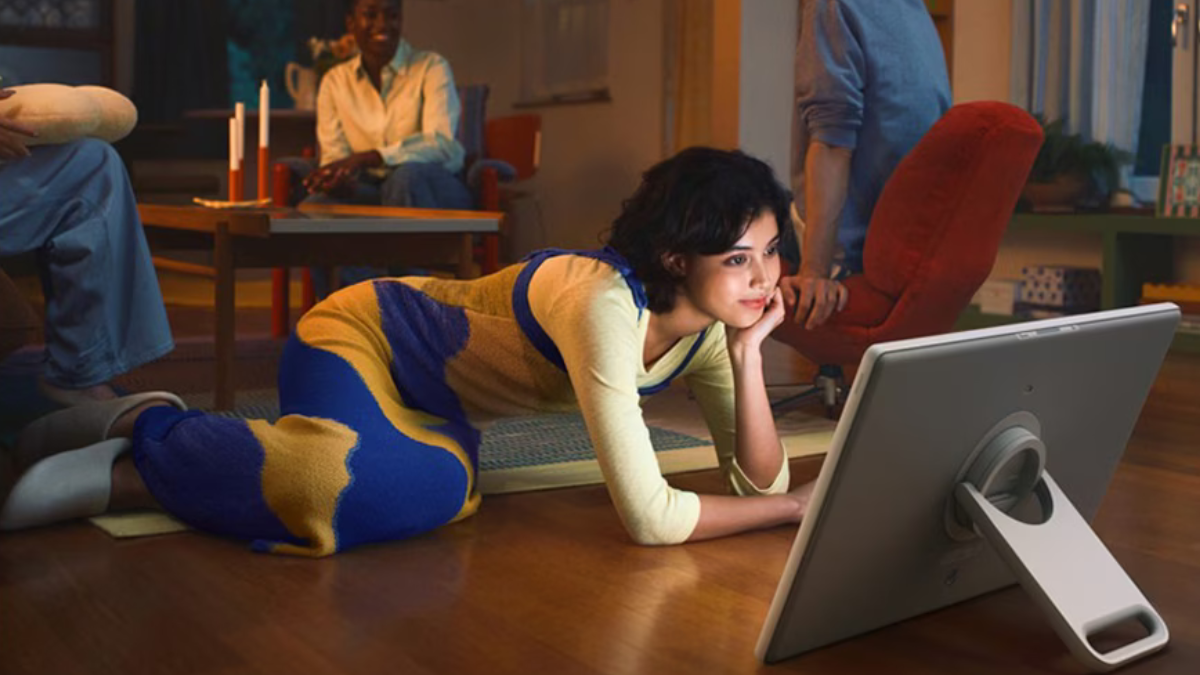 Samsung The Movingstyle: The Portable Screen on Wheels Is Finally Rolling Out. What India Needs to Know! 1 A woman lying on a living room floor using the detached 27-inch Samsung Movingstyle display with its built-in kickstand.