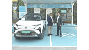 Two executives shaking hands in front of a white Tata Nexon.ev at a Shell Recharge 120kW fast-charging bay in India.
