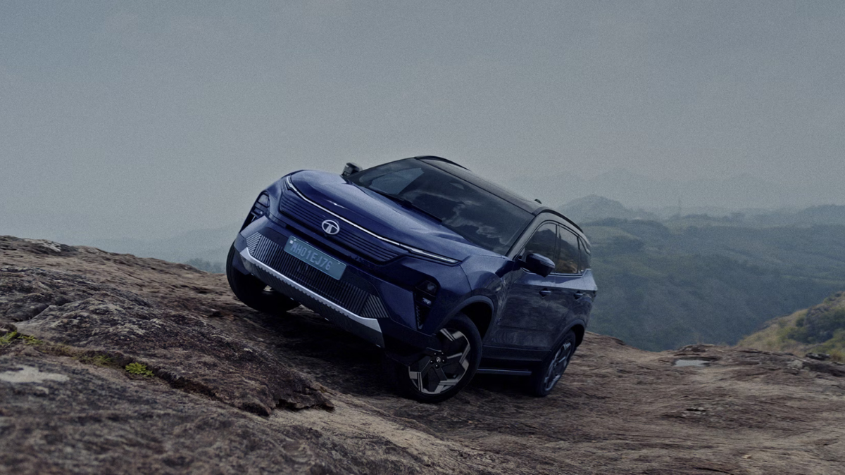 A blue Tata Harrier.ev navigating a steep rocky slope, demonstrating its off-road suspension and traction control.