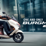 Side profile of the new 2026 Suzuki Burgman Street scooter in cream color with a rider and pillion in a modern city setting.