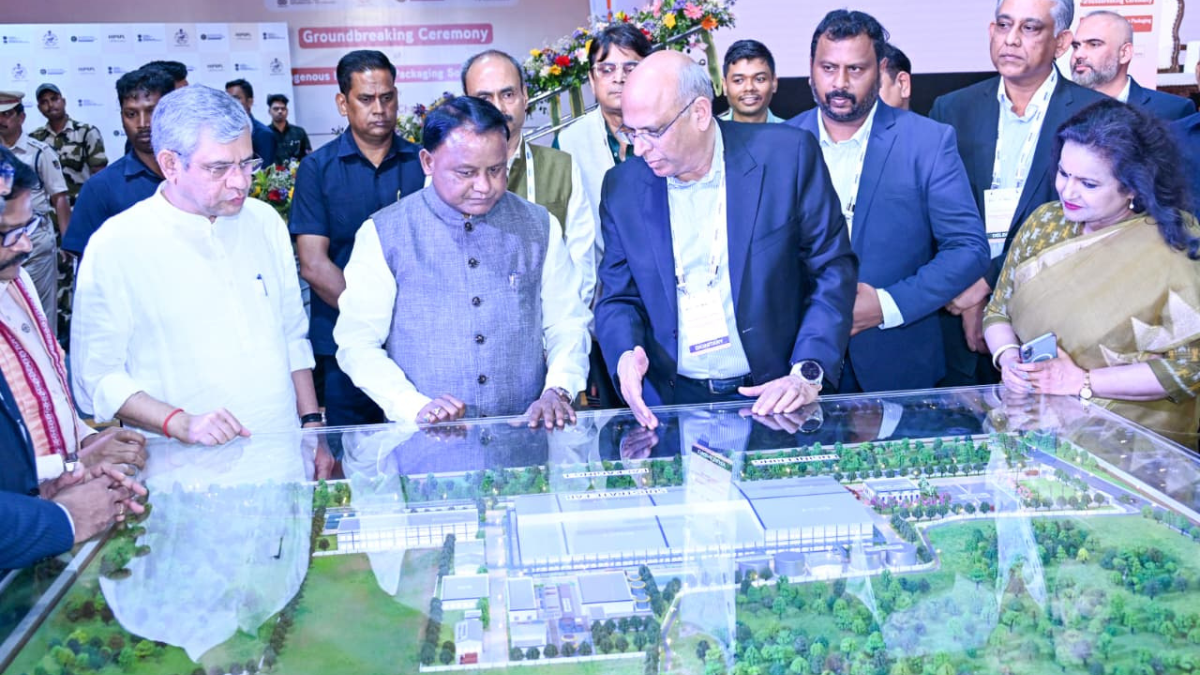 Dignitaries looking down at a detailed architectural miniature model of a large industrial facility under a glass case.