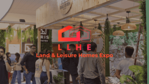 A busy exhibition booth at the Land & Leisure Homes Expo (LLHE) in Mumbai, featuring rustic wooden decor, hanging greenery...