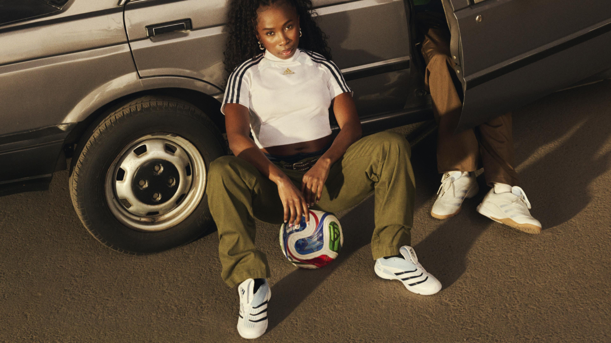 A woman sitting against a silver car with a soccer ball, wearing a white adidas crop top and the new Predator Sala sneakers.