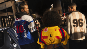 Three fans viewed from behind in a traffic jam wearing vintage-style adidas away jerseys with numbers 10 and 96 and federa...