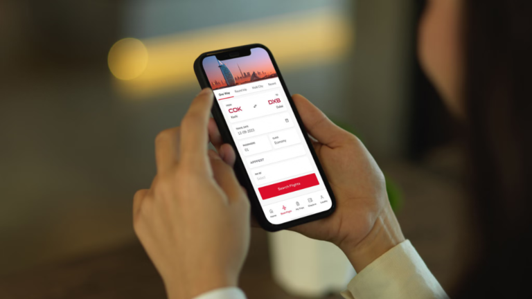 A user holding a smartphone with the high-rated Air India mobile app open to the flight booking screen for Kochi to Dubai.