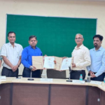 Two men holding signed documents with faculty members standing nearby for the Ayurveda innovation partnership in India.