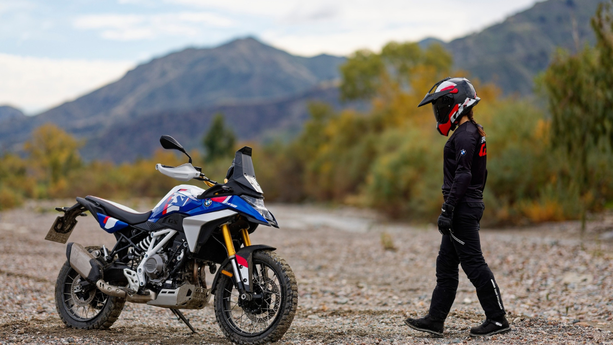 Side profile of a BMW F 450 GS Trophy variant standing on a dry riverbed, with a person in gear walking past it