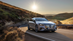Bronze Mercedes electric C-Class driving on a winding road at sunset, showcasing the upcoming 2026 India launch