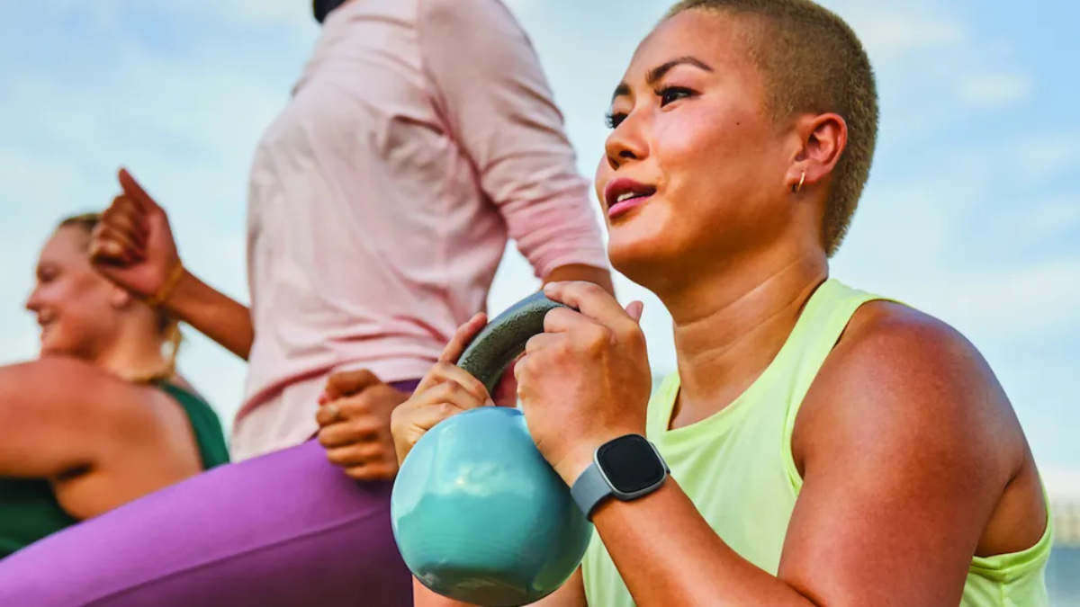 Woman holding a kettlebell outdoors wearing a Fitbit smartwatch for a personalised workout in India.