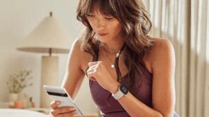 A woman in workout gear using the Fitbit AI Personal Health Coach on a Google Pixel phone to track health metrics like VO2...