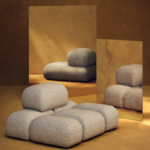 Sculptural modular Soluna lounge chair in beige textured fabric from the Kelly Wearstler x H&M HOME collection, reflected in warm-toned mirrors within a gallery setting.