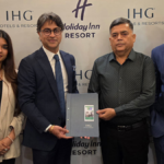 Four people standing against an IHG backdrop, holding a signed agreement folder for the new Alwar resort project.