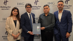 Four people standing against an IHG backdrop, holding a signed agreement folder for the new Alwar resort project.