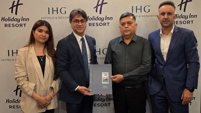Four people standing against an IHG backdrop, holding a signed agreement folder for the new Alwar resort project.